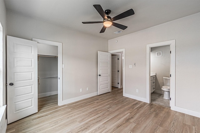 unfurnished bedroom with visible vents, a walk in closet, baseboards, ensuite bathroom, and light wood-style floors