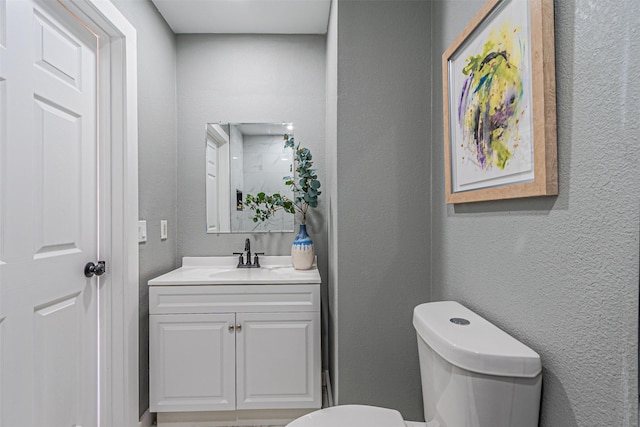 half bathroom featuring vanity, toilet, and a textured wall