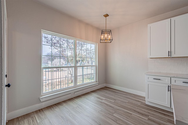 unfurnished dining area with light wood finished floors, an inviting chandelier, and baseboards