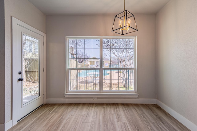 unfurnished dining area with an inviting chandelier, baseboards, and light wood finished floors