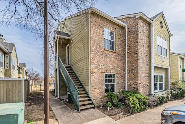 view of side of property with stairs, fence, and brick siding