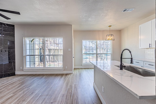 kitchen with visible vents, light wood-type flooring, light stone counters, white cabinets, and a sink