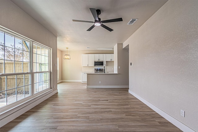 unfurnished living room with visible vents, light wood finished floors, baseboards, ceiling fan, and a textured wall