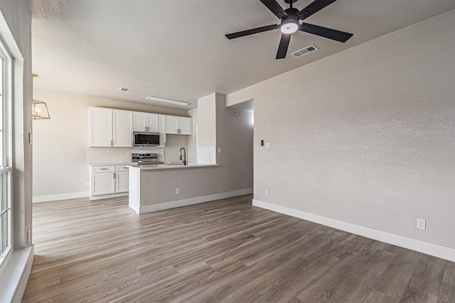 unfurnished living room featuring baseboards, visible vents, a sink, ceiling fan with notable chandelier, and light wood-type flooring