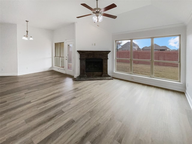 unfurnished living room featuring wood finished floors, baseboards, high vaulted ceiling, a fireplace with raised hearth, and ceiling fan with notable chandelier