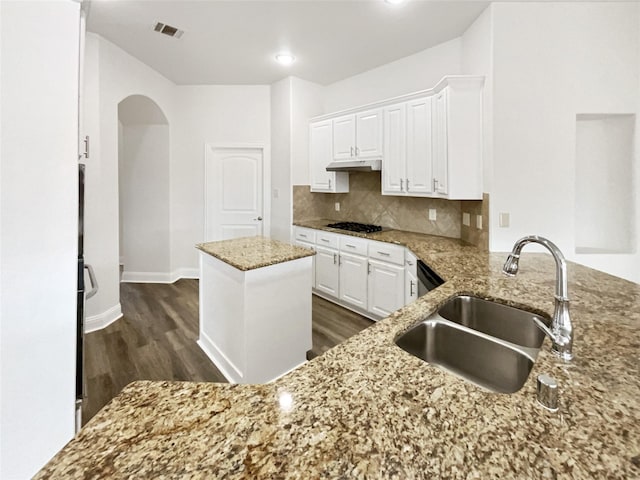 kitchen with light stone counters, decorative backsplash, arched walkways, white cabinetry, and a sink