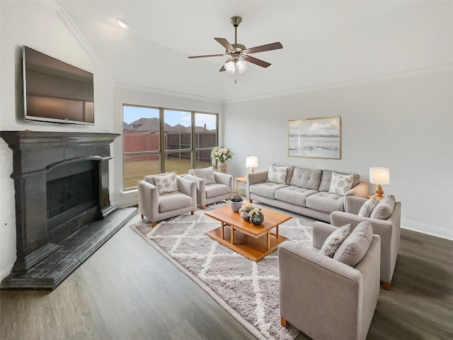 living area with a fireplace with raised hearth, crown molding, baseboards, wood finished floors, and a ceiling fan