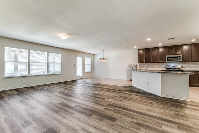 kitchen featuring dark brown cabinetry, decorative backsplash, stainless steel appliances, and light wood-type flooring