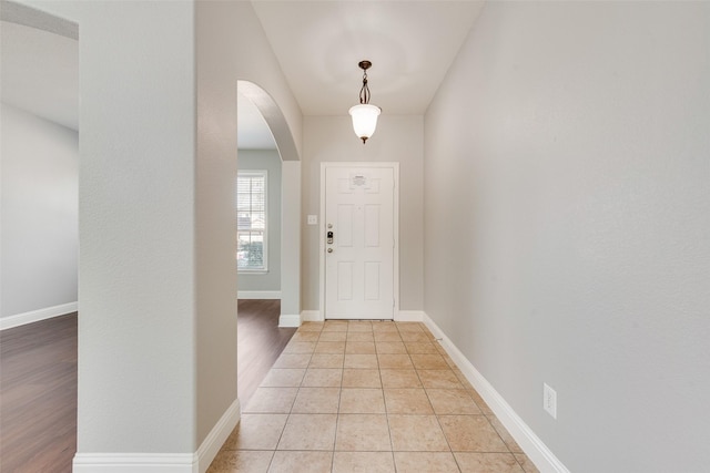 entrance foyer featuring light tile patterned floors, arched walkways, and baseboards