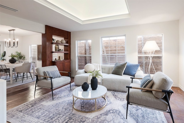 living area with visible vents, built in features, baseboards, a chandelier, and wood finished floors