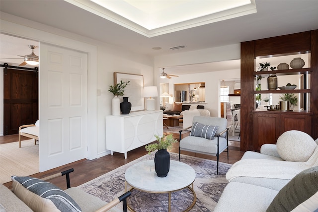 living area featuring wood finished floors, a ceiling fan, visible vents, and a barn door