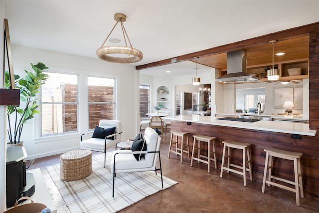 kitchen with black gas stovetop, light countertops, a kitchen bar, range hood, and a sink