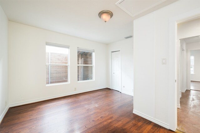 spare room featuring wood finished floors, attic access, baseboards, and visible vents