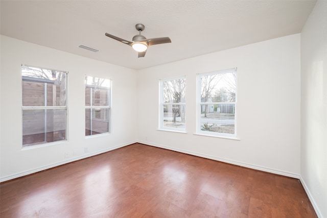 spare room with wood finished floors, a ceiling fan, visible vents, and a healthy amount of sunlight
