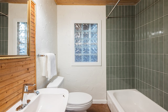 full bath with baseboards, a textured wall, bathing tub / shower combination, toilet, and a sink
