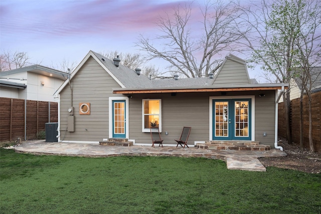 back of house at dusk with entry steps, a yard, a fenced backyard, a patio, and french doors