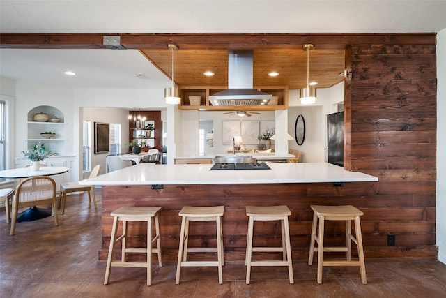 kitchen with built in features, a kitchen bar, island exhaust hood, light countertops, and decorative light fixtures