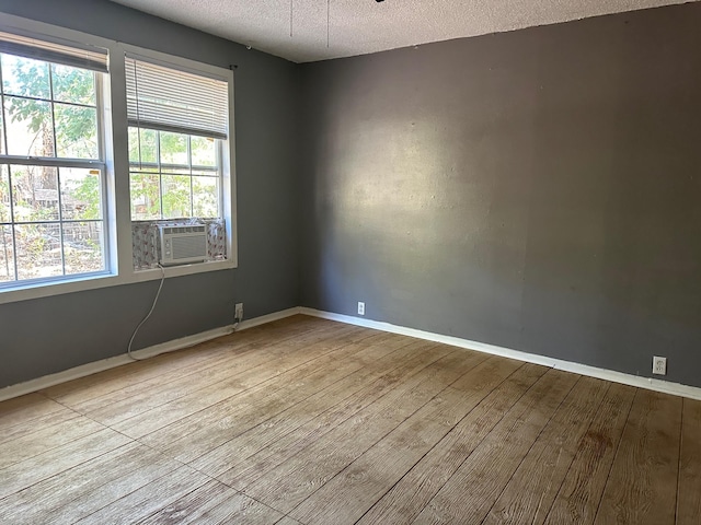 spare room with cooling unit, wood finished floors, baseboards, and a textured ceiling