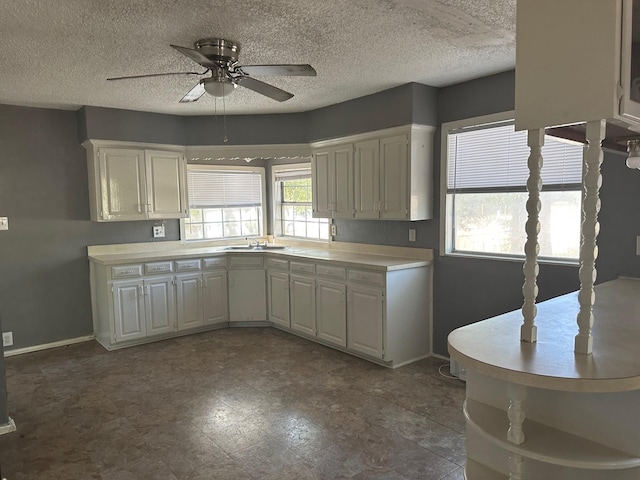 kitchen featuring light countertops, white cabinets, a textured ceiling, a ceiling fan, and a sink