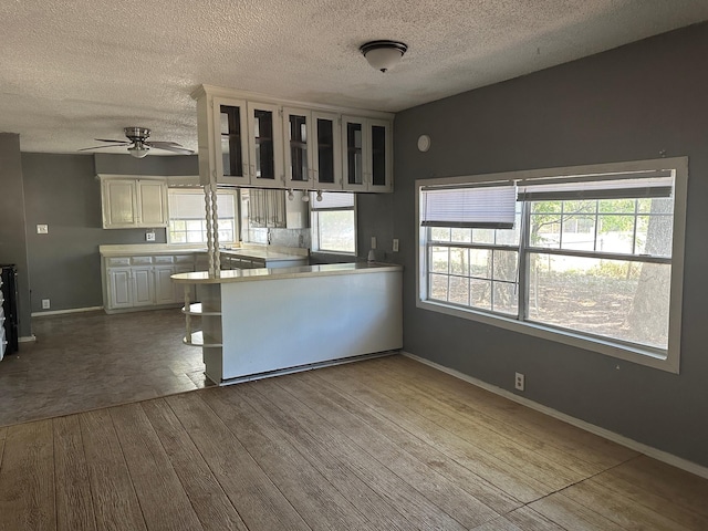 kitchen featuring wood-type flooring, white cabinets, light countertops, glass insert cabinets, and ceiling fan