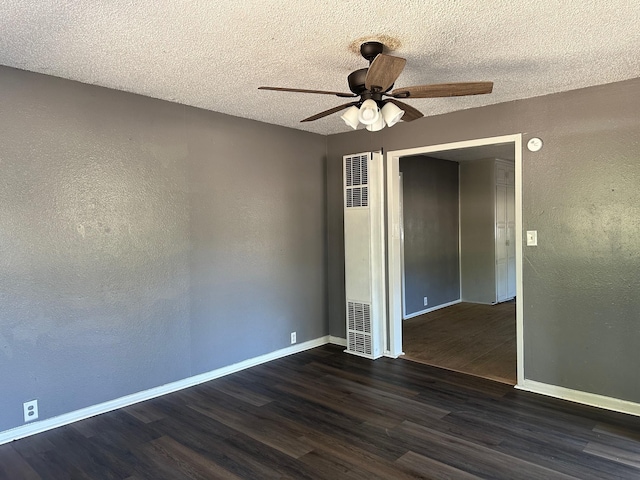 unfurnished room featuring a ceiling fan, dark wood-style floors, baseboards, a heating unit, and a textured wall