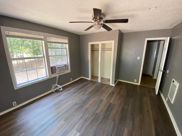 unfurnished bedroom with cooling unit, a textured ceiling, baseboards, and dark wood-style flooring