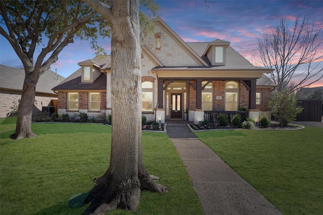 view of front of property featuring a front lawn, brick siding, stone siding, and a shingled roof