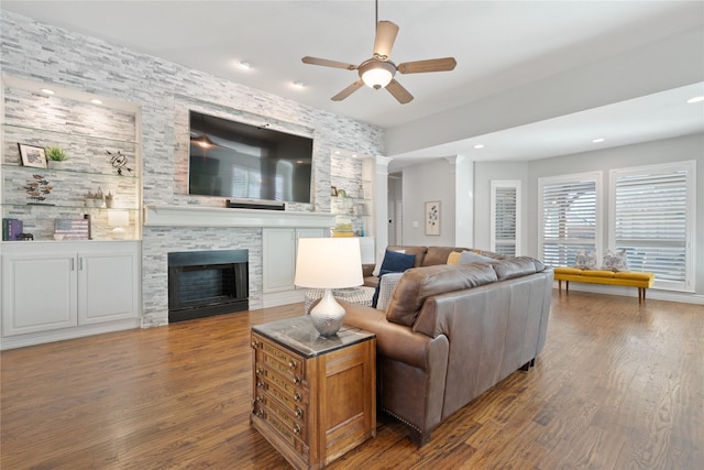 living room with built in features, a stone fireplace, recessed lighting, wood finished floors, and a ceiling fan