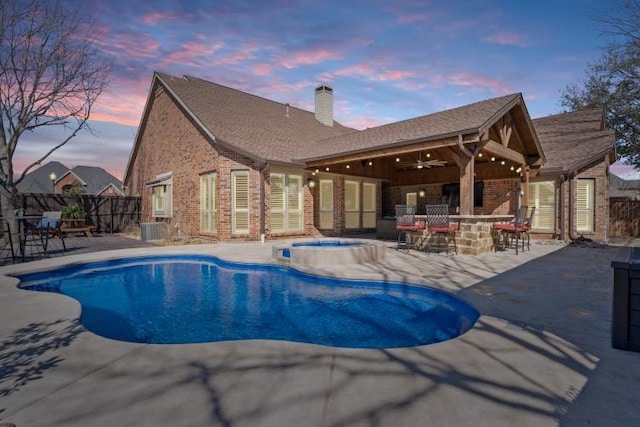 pool at dusk featuring an in ground hot tub, fence, outdoor dry bar, and a patio area