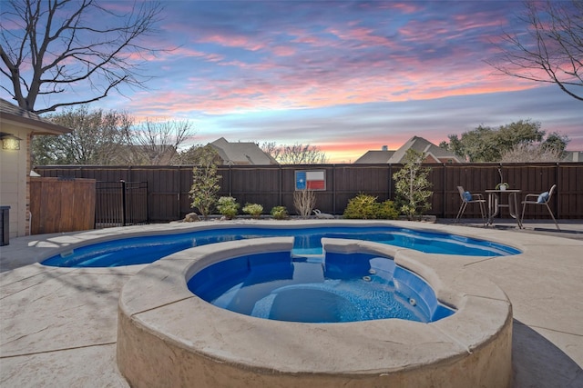 pool at dusk with a patio area, an in ground hot tub, and a fenced backyard