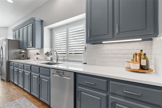 kitchen with a sink, appliances with stainless steel finishes, wood finished floors, and light countertops