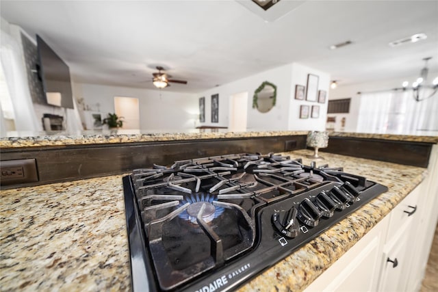 interior details featuring light stone counters, white cabinets, black gas stovetop, and ceiling fan