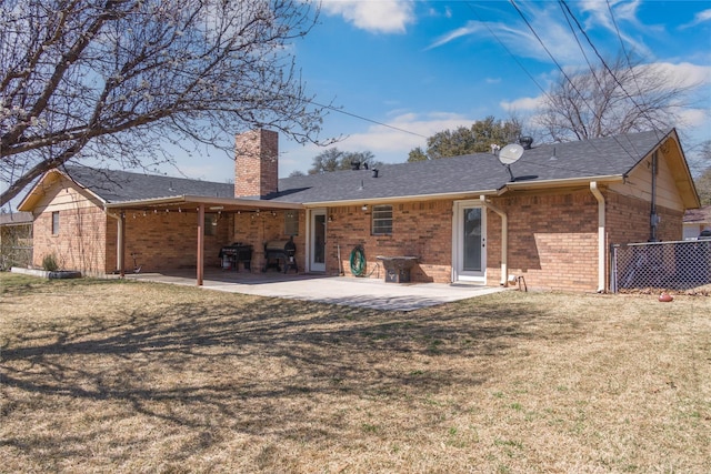 back of property featuring brick siding, a patio area, a lawn, and a chimney