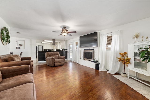 living room with a ceiling fan, a brick fireplace, wood finished floors, and visible vents