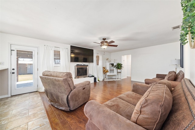 living area with baseboards, visible vents, ceiling fan, a glass covered fireplace, and light wood-type flooring