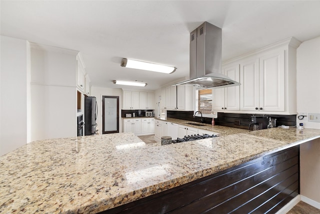 kitchen featuring island exhaust hood, a sink, appliances with stainless steel finishes, white cabinets, and light stone countertops