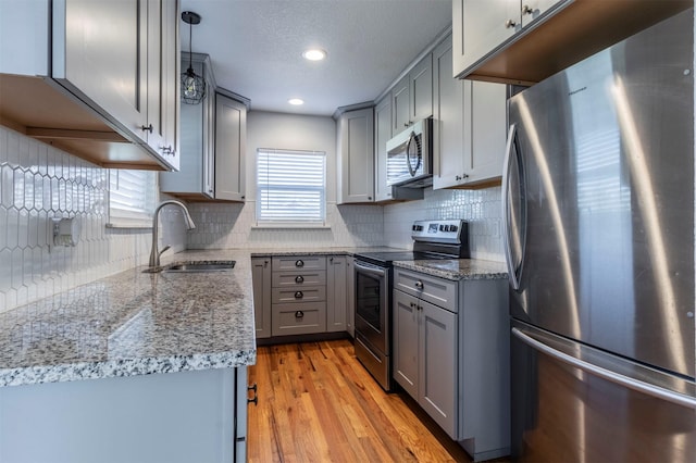 kitchen with light stone counters, appliances with stainless steel finishes, gray cabinetry, and a sink