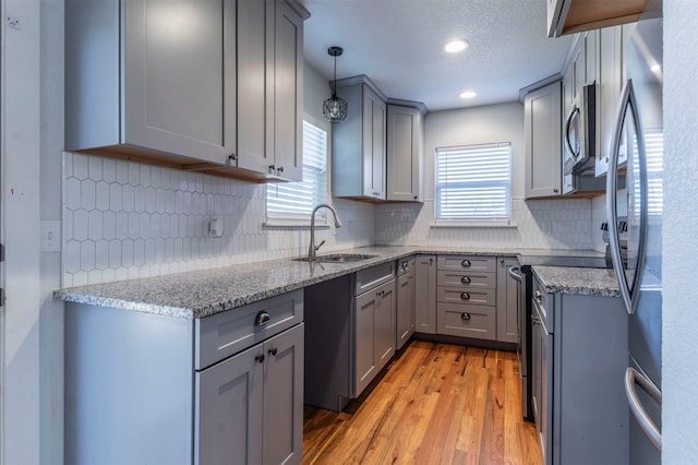 kitchen with gray cabinets, a sink, stainless steel appliances, light wood finished floors, and light stone countertops