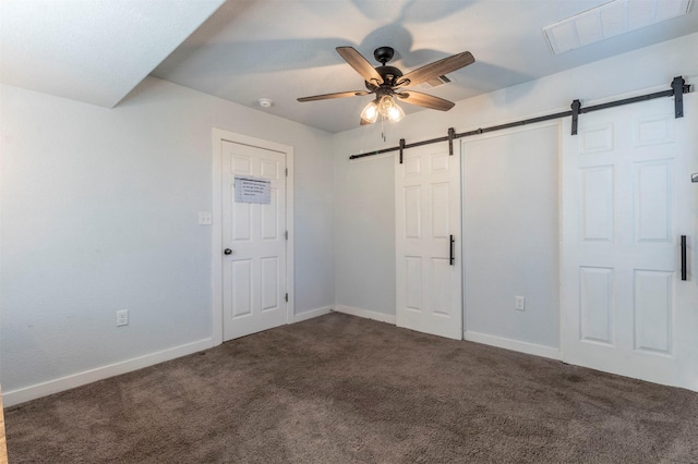 unfurnished bedroom featuring dark colored carpet, a barn door, baseboards, and visible vents