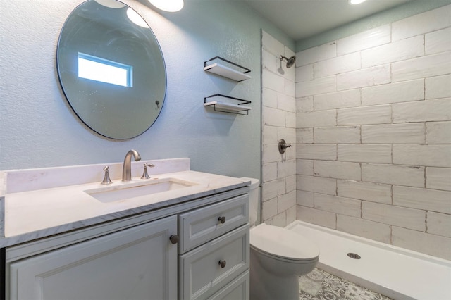 full bath featuring vanity, toilet, a textured wall, and a tile shower