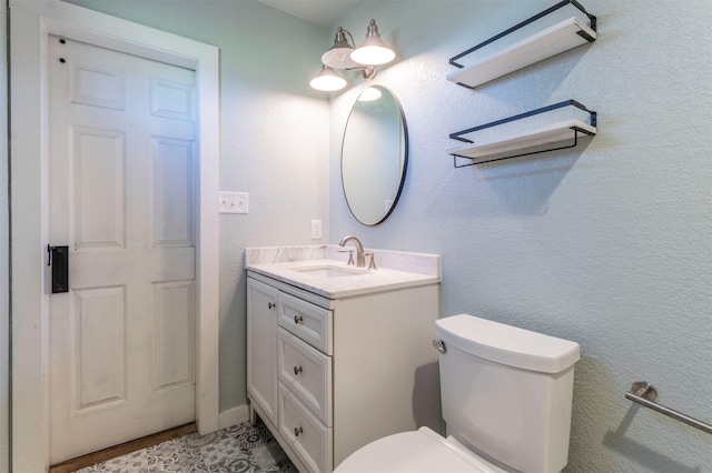 bathroom with vanity, toilet, and a textured wall