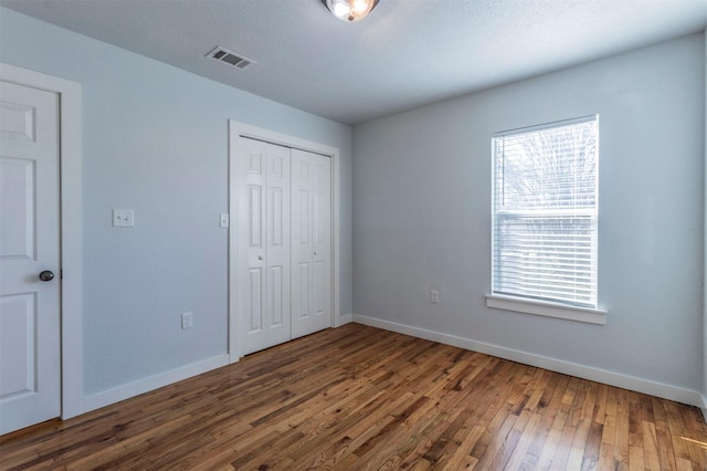 unfurnished bedroom featuring a closet, baseboards, visible vents, and wood-type flooring