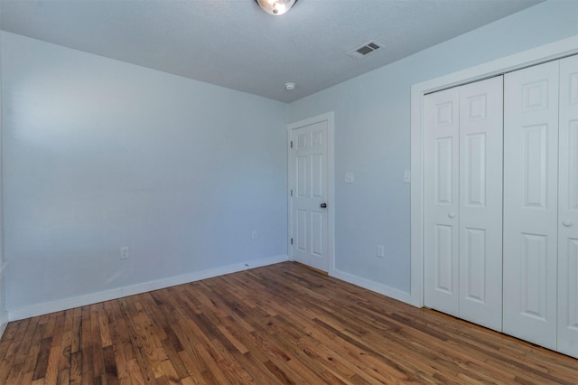 unfurnished bedroom with a closet, visible vents, baseboards, and wood finished floors