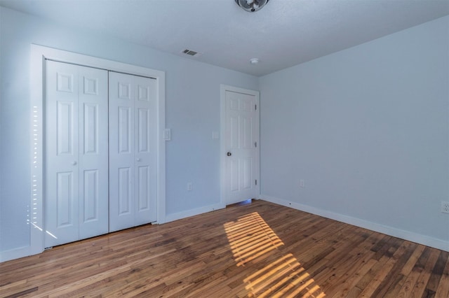 unfurnished bedroom with a closet, visible vents, baseboards, and wood finished floors