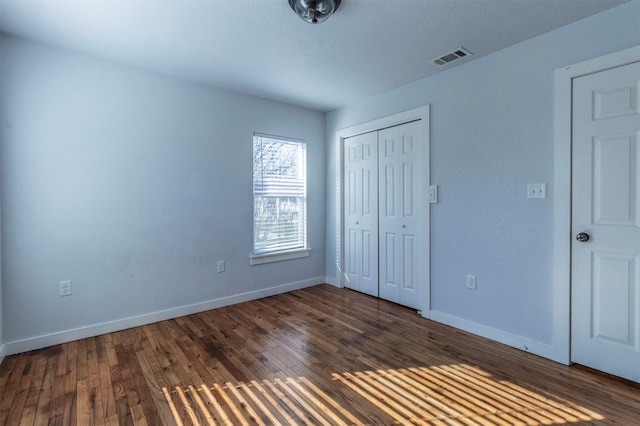 unfurnished bedroom featuring dark wood finished floors, visible vents, a closet, and baseboards