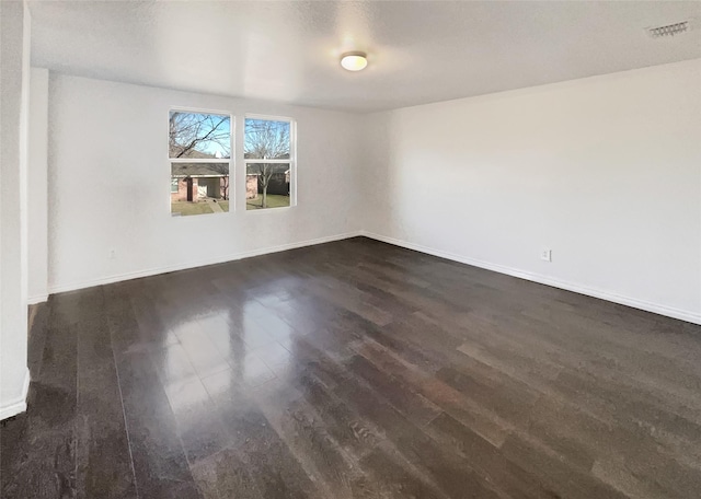 spare room featuring dark wood-type flooring, visible vents, and baseboards