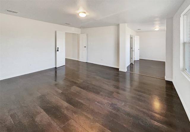 spare room featuring visible vents, dark wood-type flooring, and baseboards