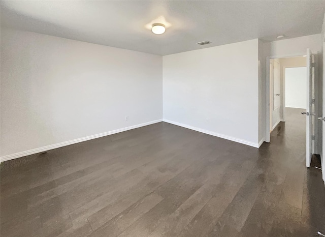 empty room featuring visible vents, baseboards, and dark wood-style flooring