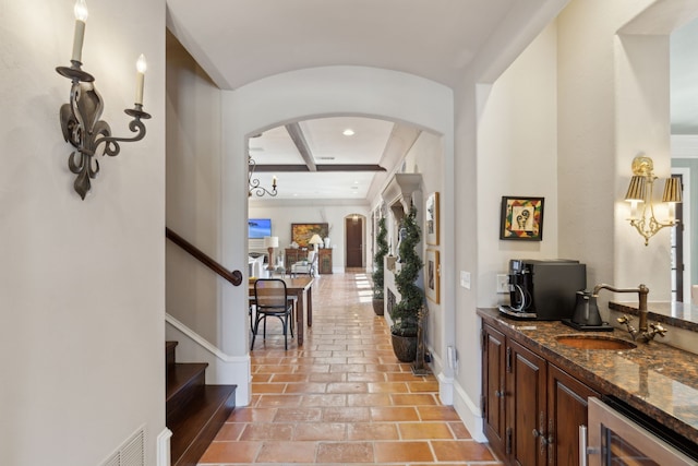 corridor with a sink, wine cooler, arched walkways, baseboards, and stairs