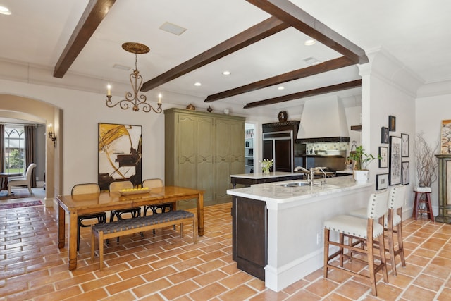 kitchen with premium range hood, a peninsula, arched walkways, paneled fridge, and a sink